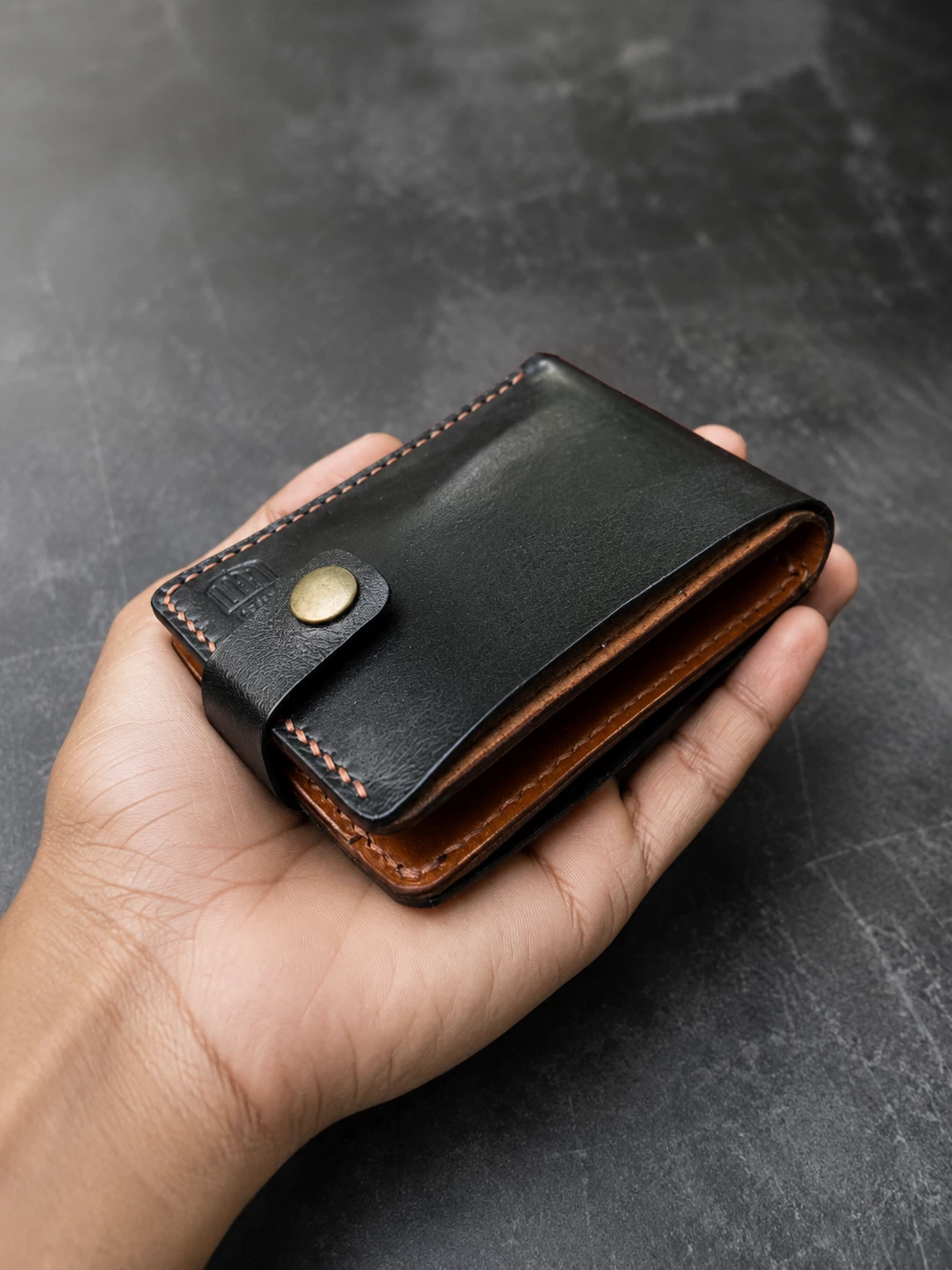 Slim black leather wallet held in hand showing compact everyday carry size and handcrafted finish.