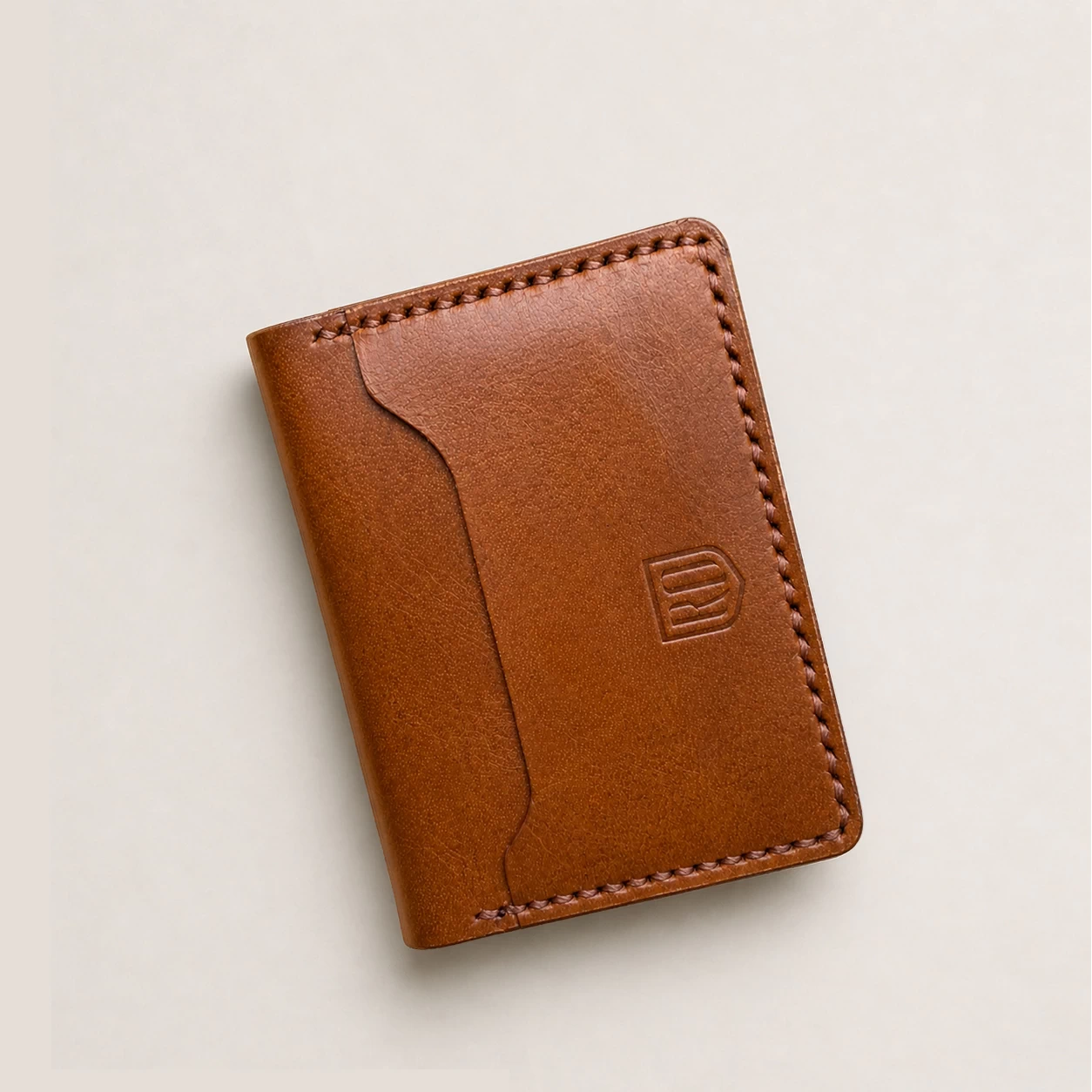 chestnut brown minimalist bifold leather card holder with exposed card slot and hand-stitched edges.