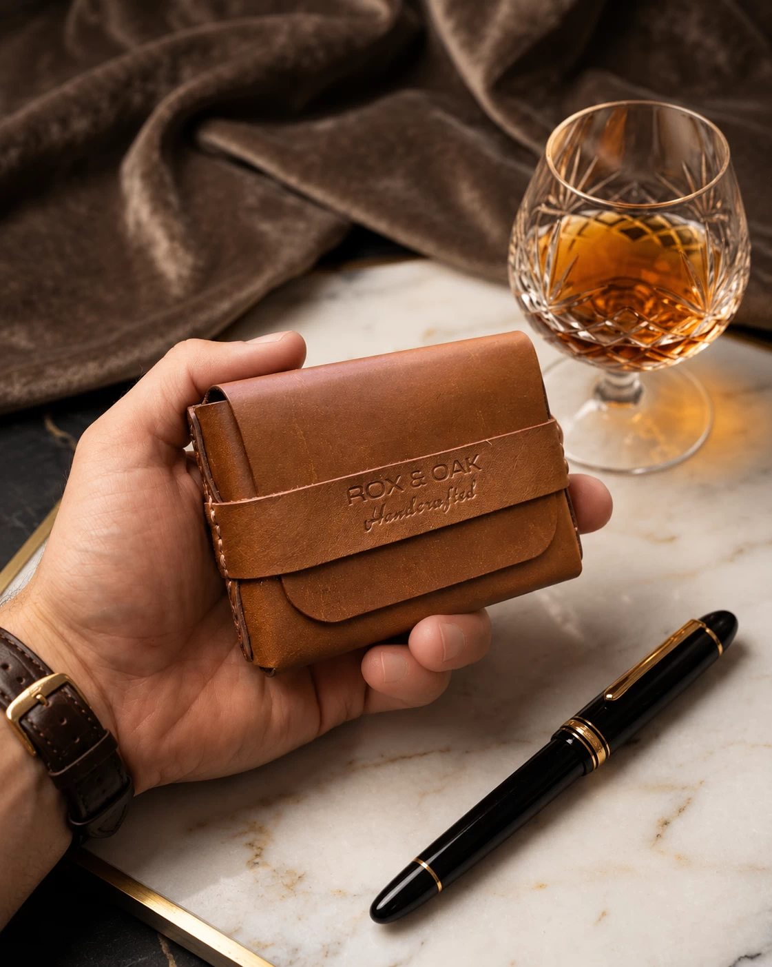 Hand holding the ROX & OAK Oaklet chestnut brown leather card holder wallet beside a pen Copy alt text